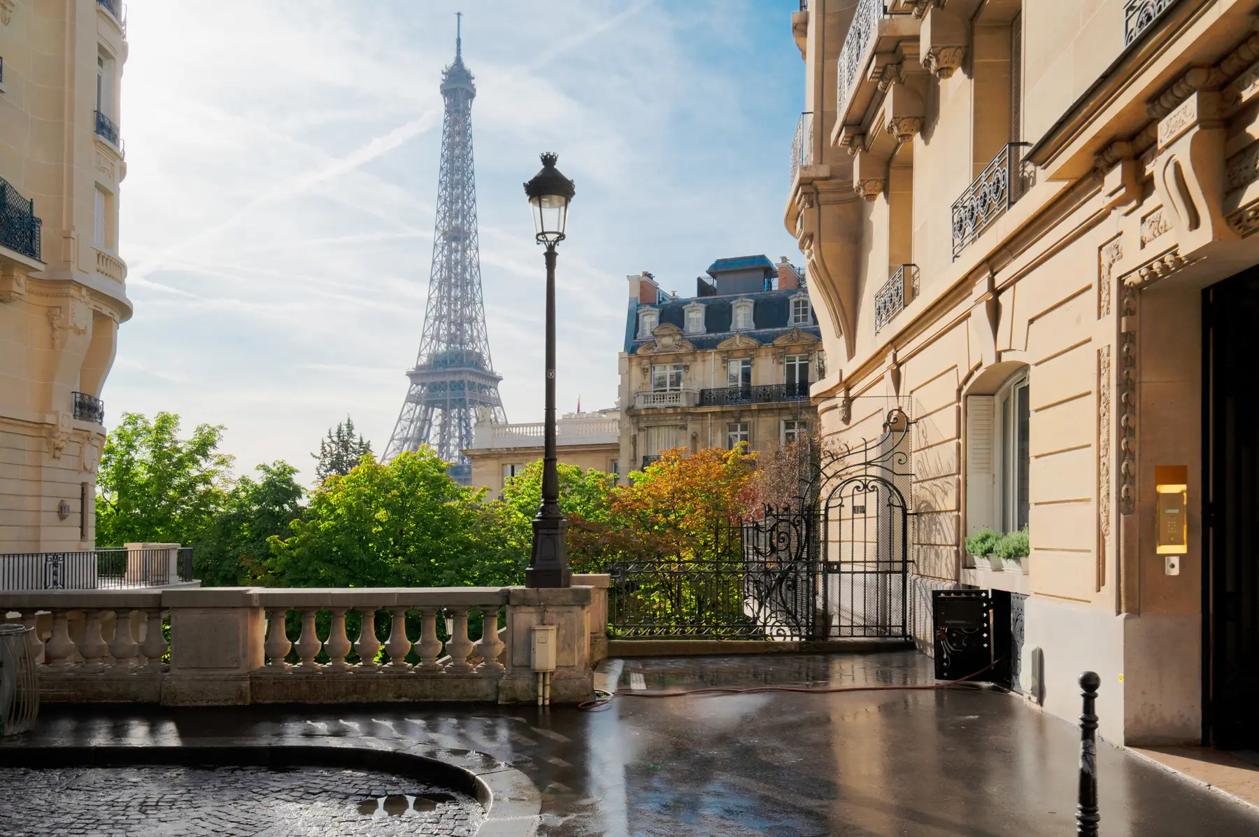 A Paris street with the Eiffel Tower in the distance, seen between Haussmann buildings.
